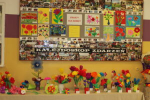 Prace plastyczne uczniów wykonane na konkurs Kwiaty dla Kobiet. Są piękne, kolorowe duże i małe, barwne, wiosenne w swoim wyglądzie. Ustawione są na stoliku aby bardziej były widoczne z każdej strony