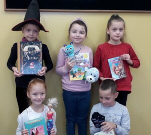 Na tle jasnej ściany stoją uczniowie klasy IIa w rękach trzymają książki.