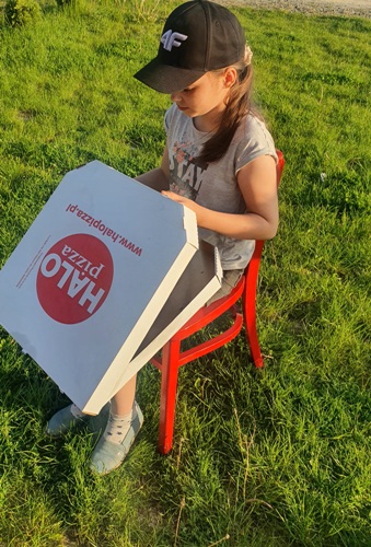 Dziewczynka siedząca na czerwonym krześle z pudełkiem pizzy
