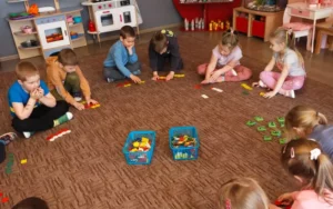 Przedszkolaki siedzące w kółku na dywanie rozwiązują działania matematyczne w zakresie 10