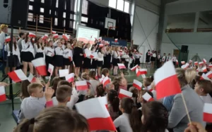 Społeczność szkolna machająca flagami narodowymi w rytm śpiewanego utworu