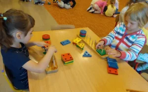 Dzieci z grupy przedszkolnej wkładają różne figury geometryczne w odpowiednie miejsca