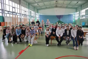 Uczniowie siedzący na ławkach w nowo otrzymanych kaskach rowerowych.